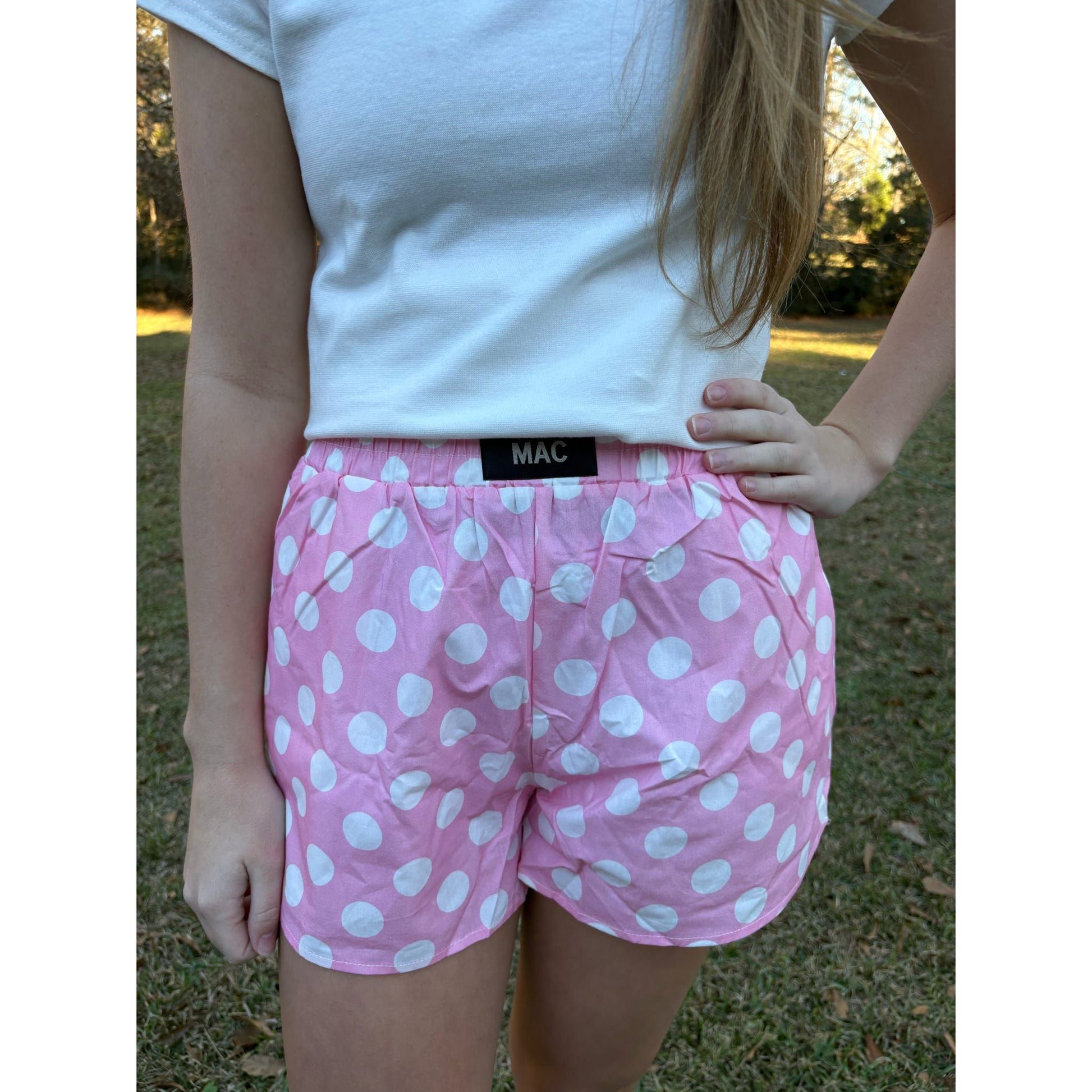 Person wearing pink polka dot shorts with a white top outdoors.