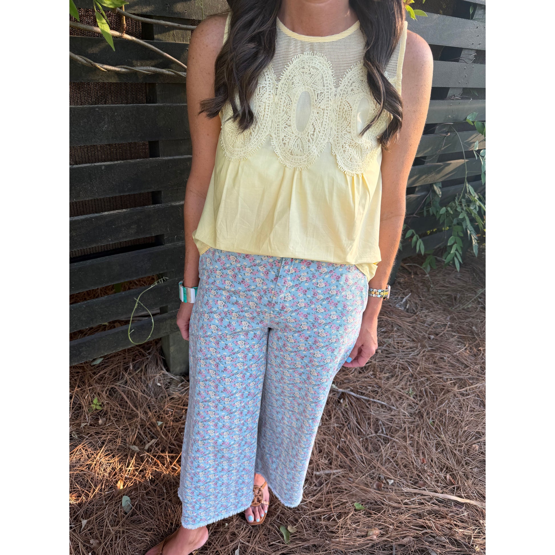 Woman wearing a light yellow top with lace details and floral pants, standing outdoors.