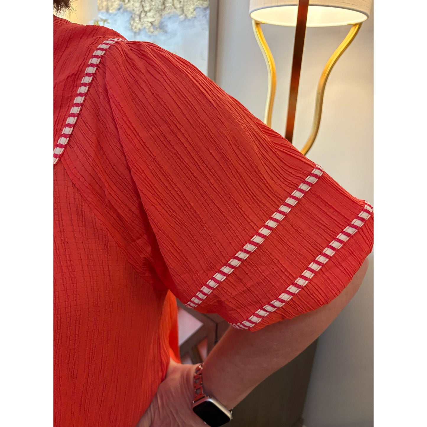 Red dress with white trim worn by a person, indoors with a lamp in the background.