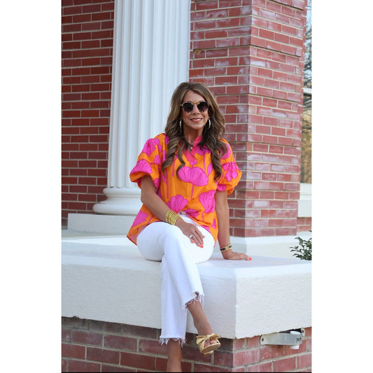 Woman in a colorful shirt and white pants sitting on steps with a brick building in the background