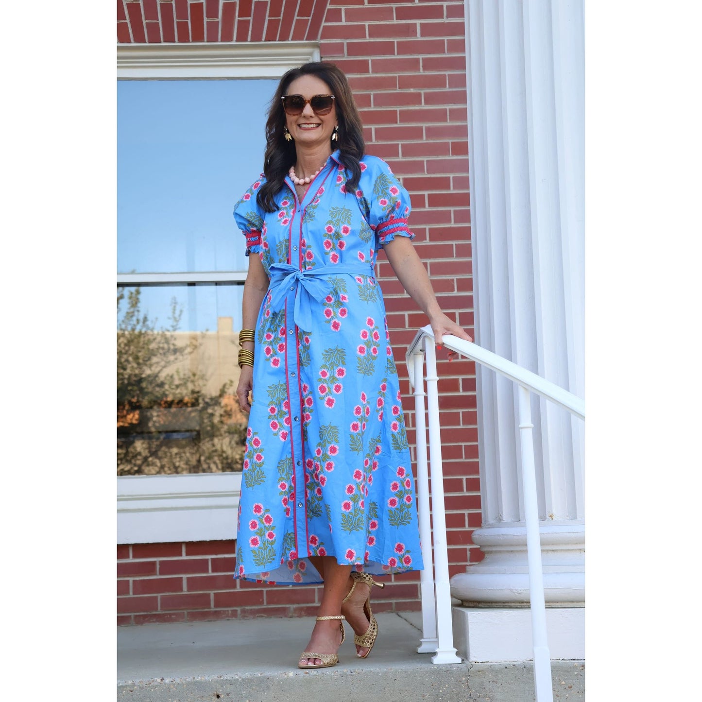 Woman in a blue floral dress standing on a porch.