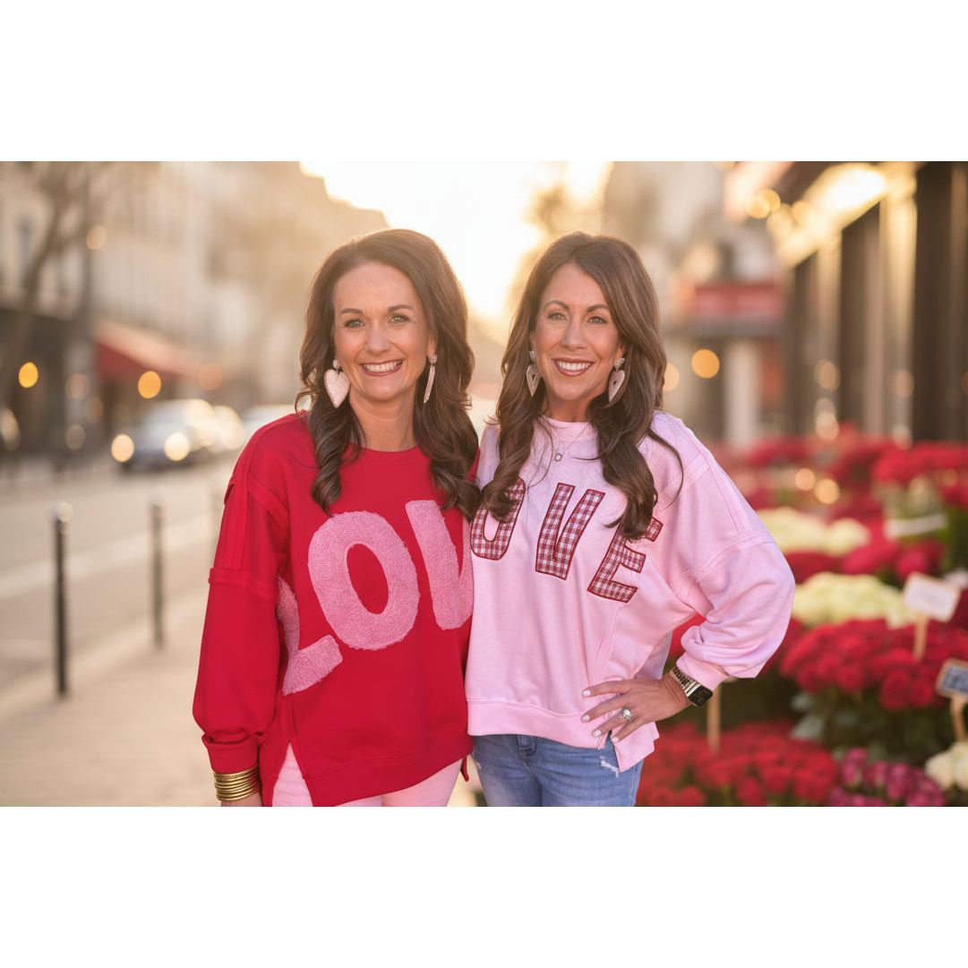 Two women wearing 'LOVE' sweatshirts standing outside on the streets with a flower market in the background.