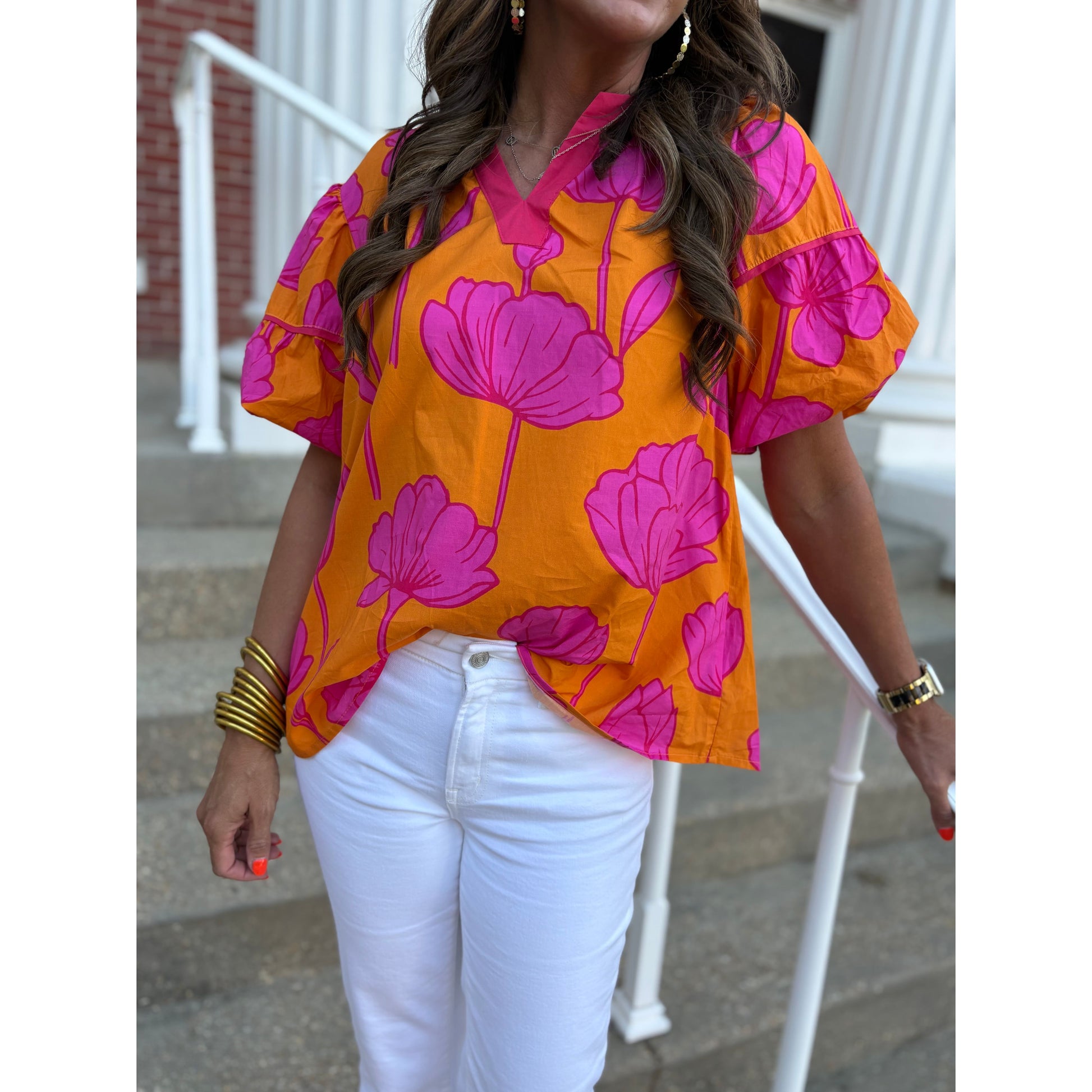 Person wearing a bright orange and pink floral blouse with white pants outdoors.