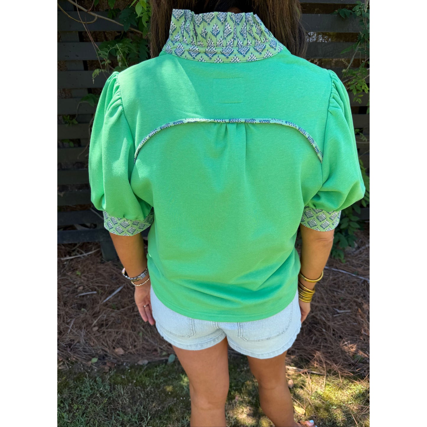 Green blouse with patterned collar and cuffs worn by a person outdoors.