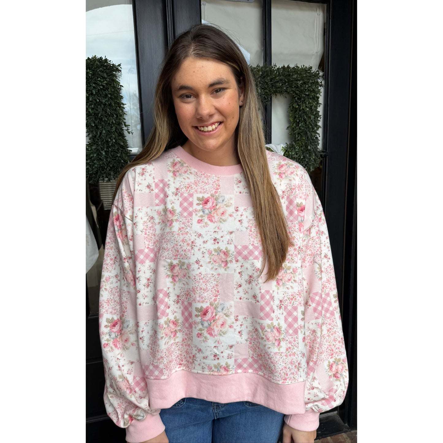 woman standing in front of door wearing a white and pink floral sweatshirt