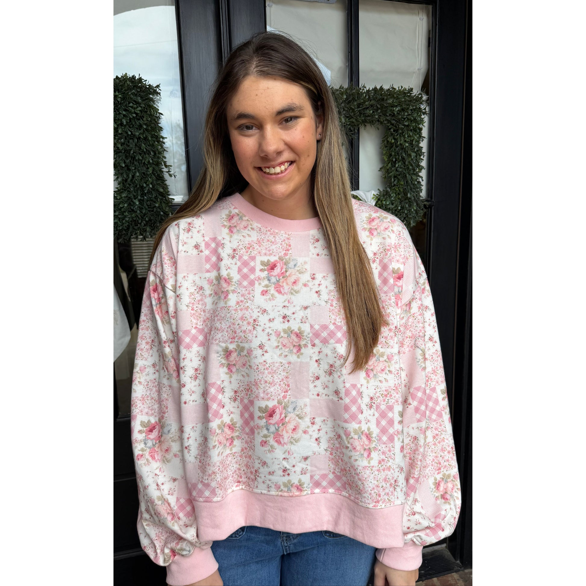 woman standing in front of door wearing a white and pink floral sweatshirt