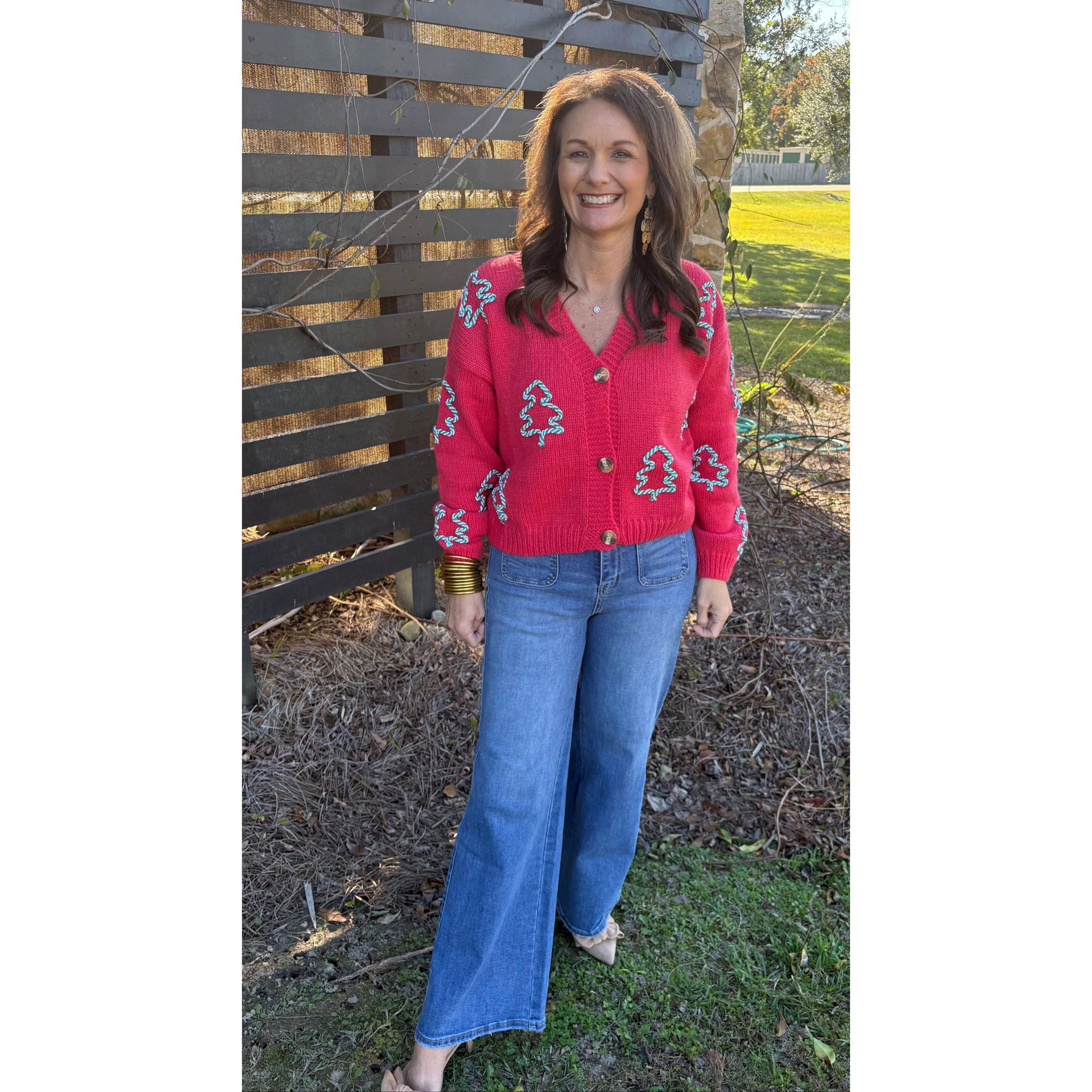 Woman wearing a red sweater with tree patterns and blue jeans standing outdoors.