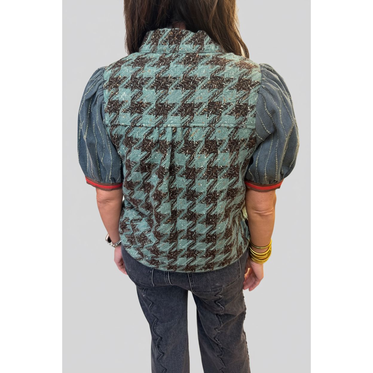 A person shown from the back wearing a quilted houndstooth vest with puff sleeves and dark gray jeans in an indoor room setting.