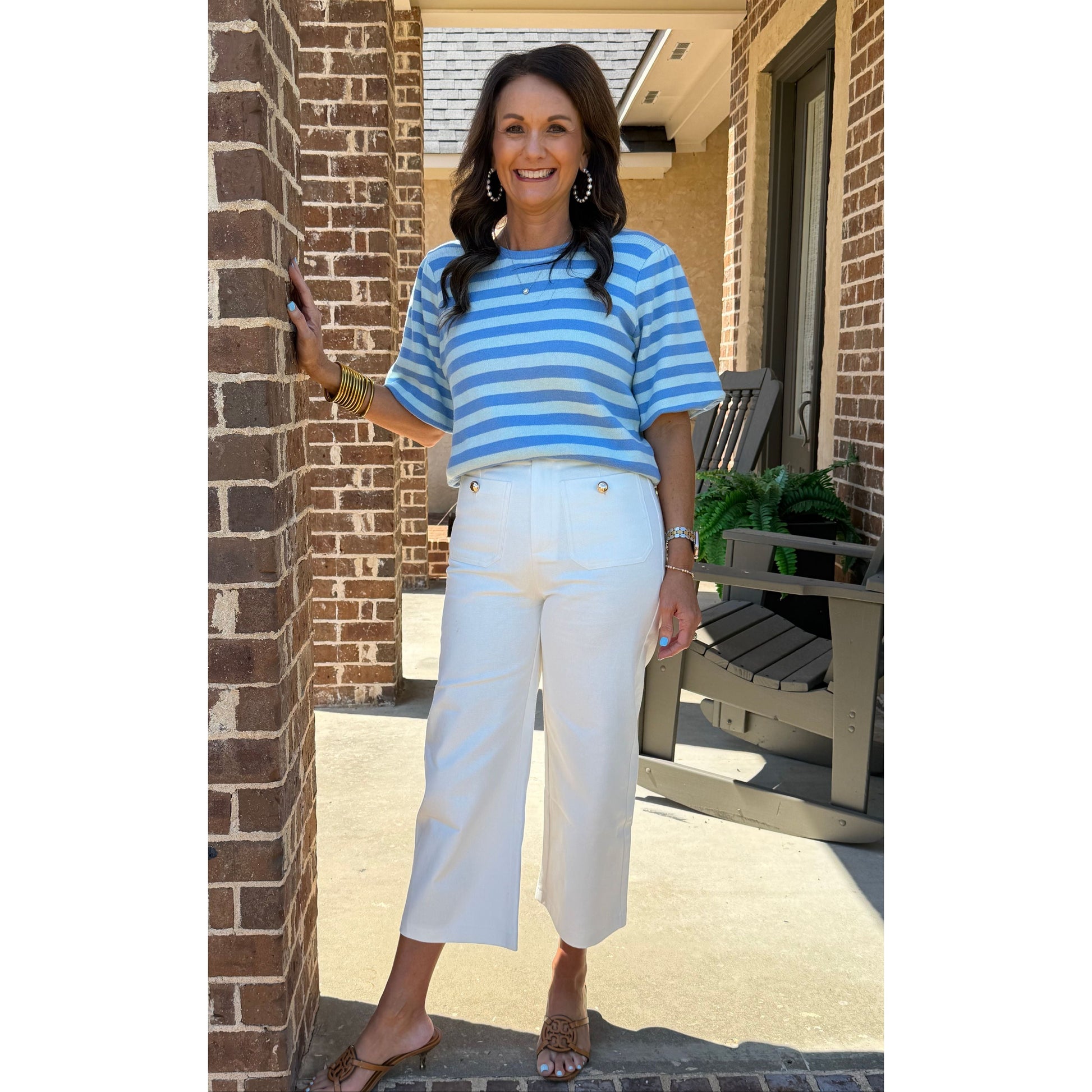 Woman wearing a blue and white striped shirt and white pants standing on a brick patio.