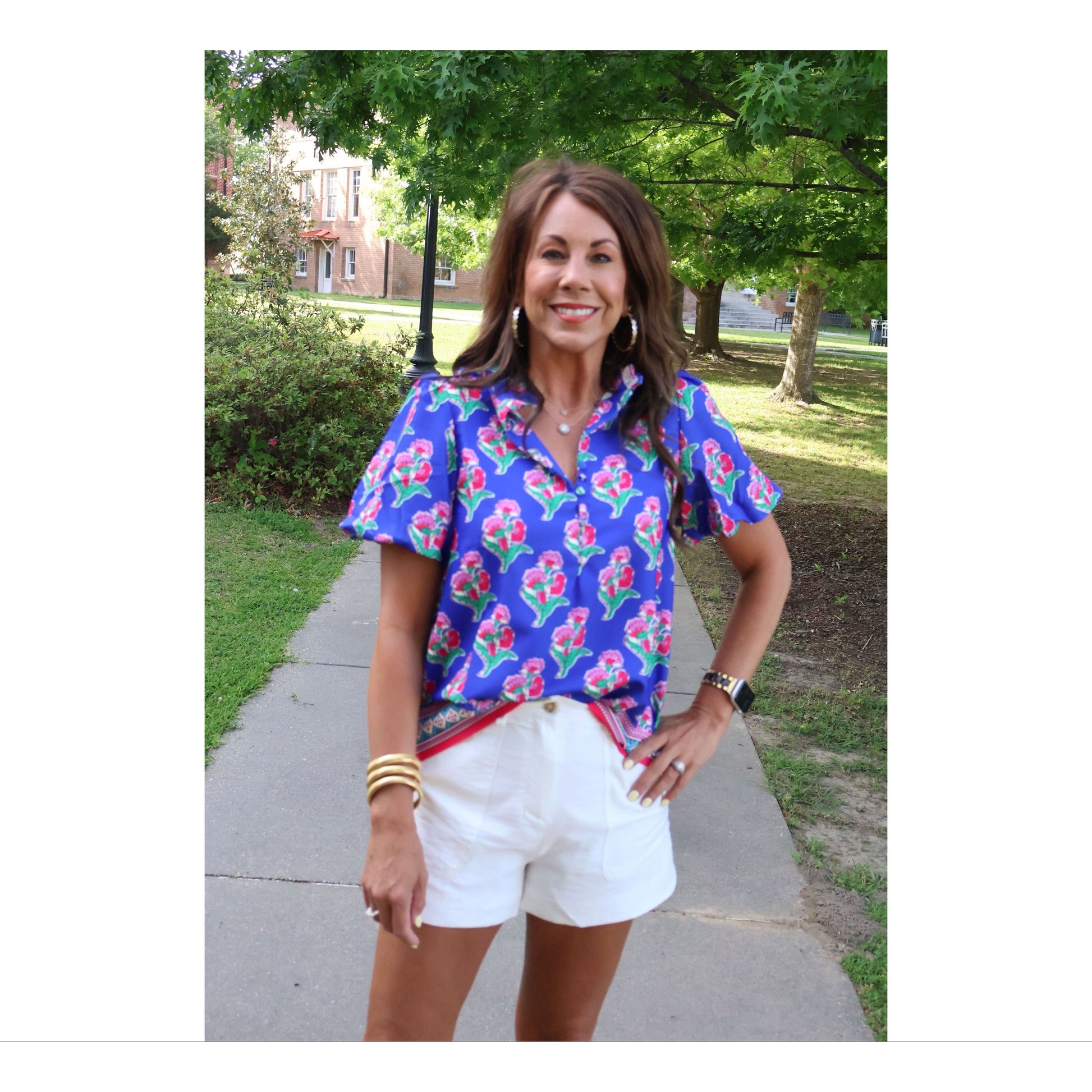 Woman wearing a colorful floral blouse and white shorts standing outdoors on a sunny day.