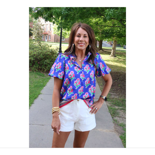 Woman wearing a colorful floral blouse and white shorts standing outdoors on a sunny day.
