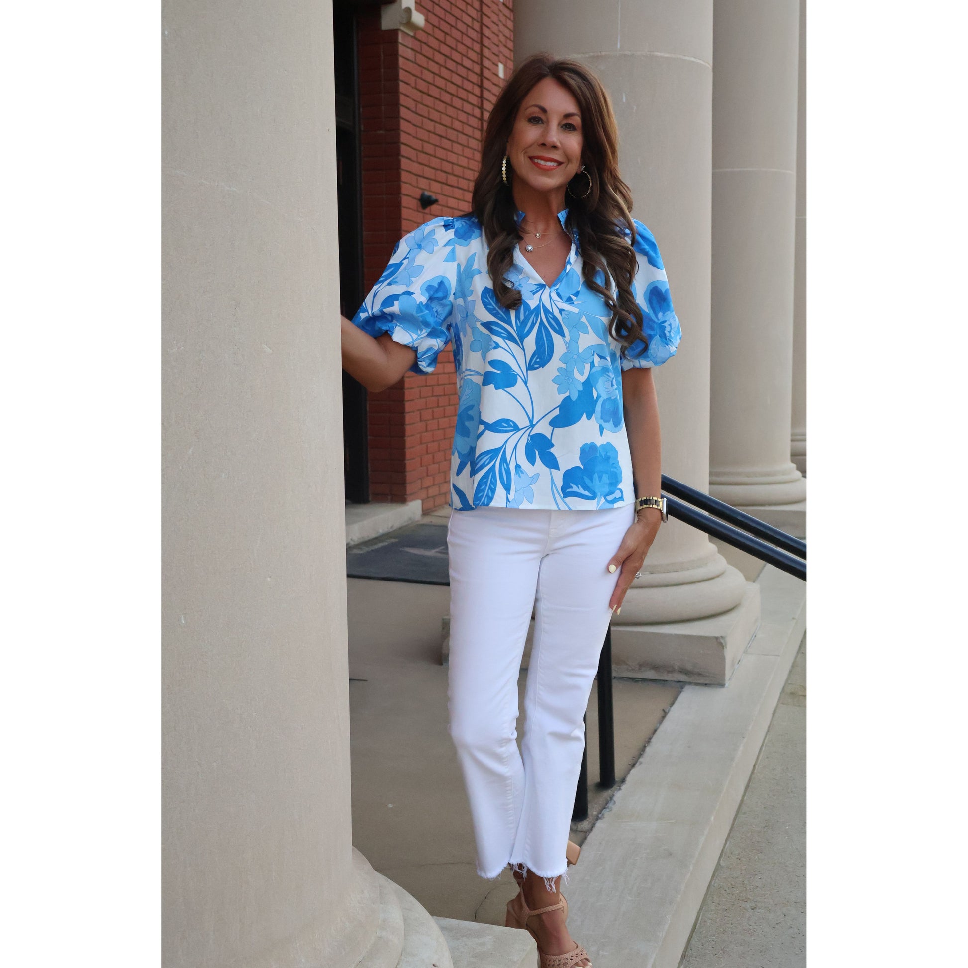 Woman wearing a blue floral dress and white pants standing indoors.