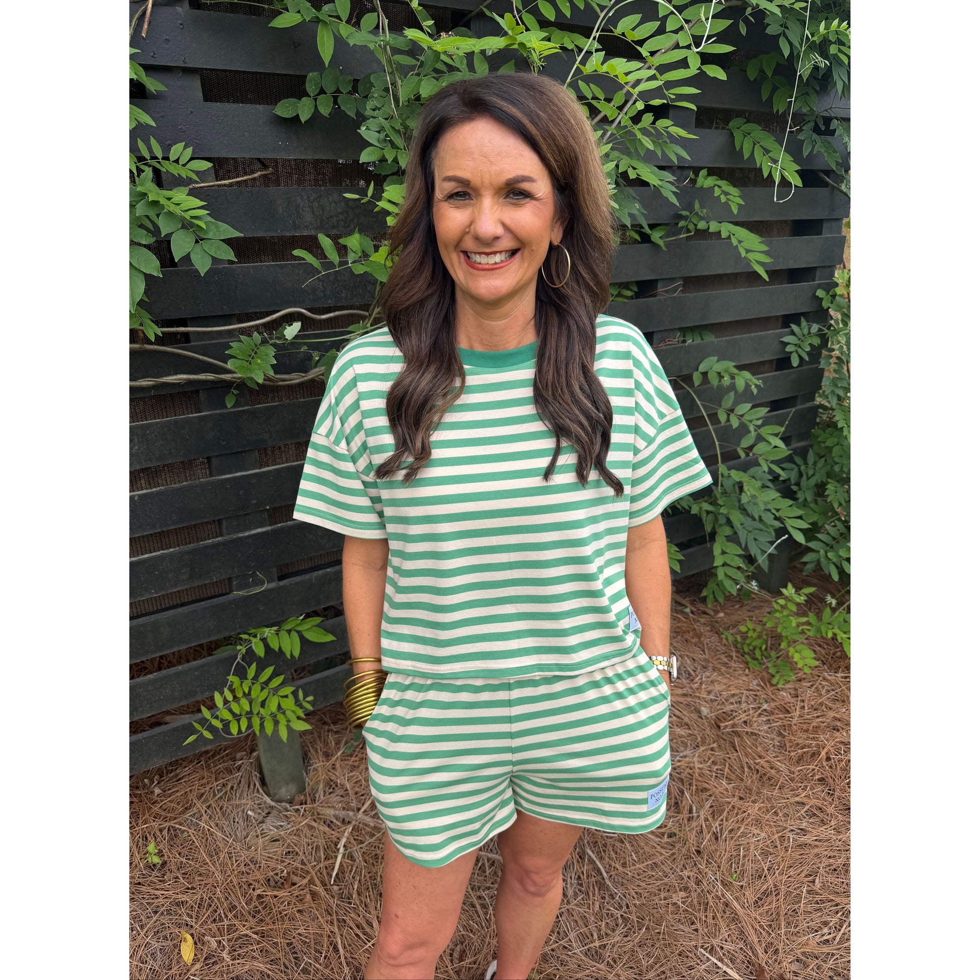 Woman wearing a green and white striped dress standing outdoors with plants around.
