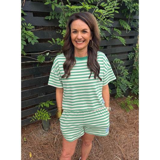 Woman wearing a green and white striped dress standing outdoors with plants around.