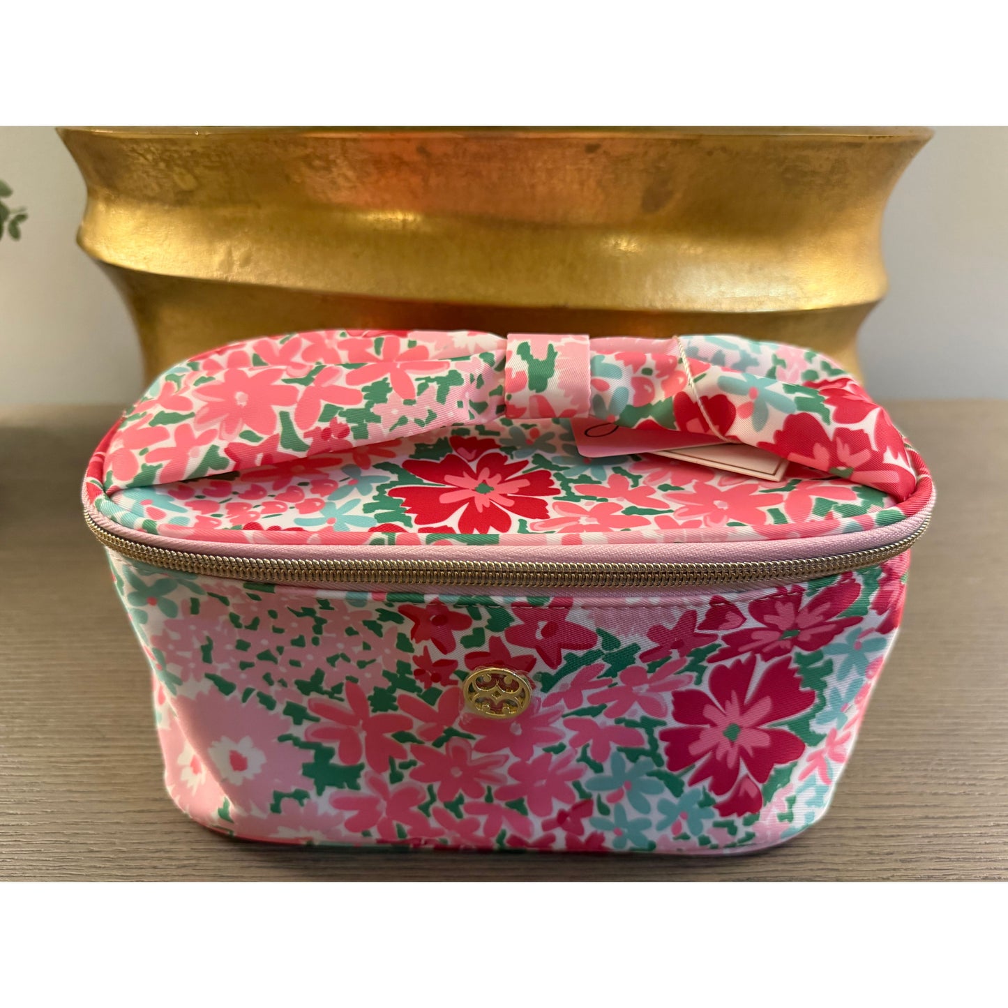 Floral-patterned cosmetic bag on a wooden surface with a gold decorative object in the background.