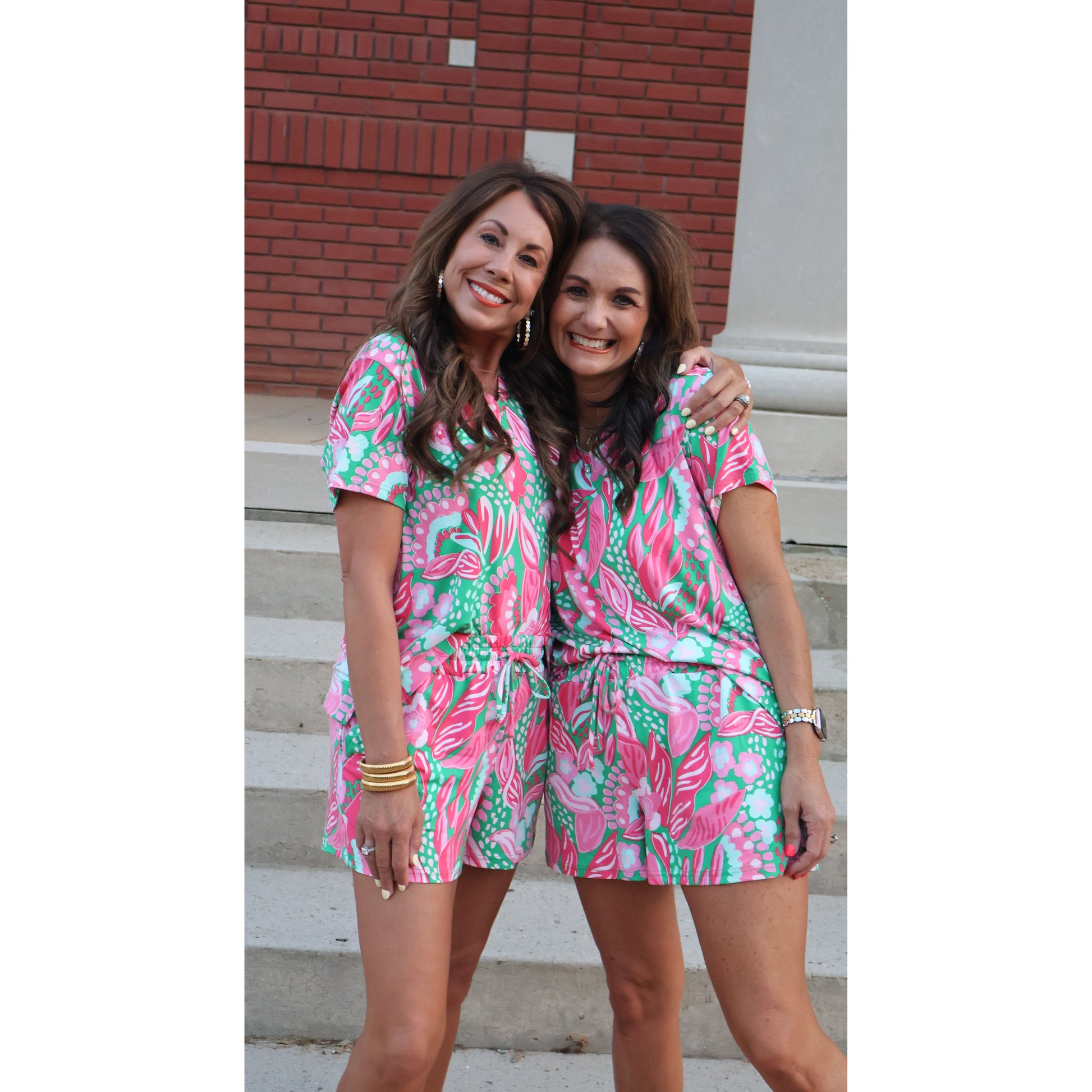 Two women wearing matching pink and green floral outfits standing on a staircase.
