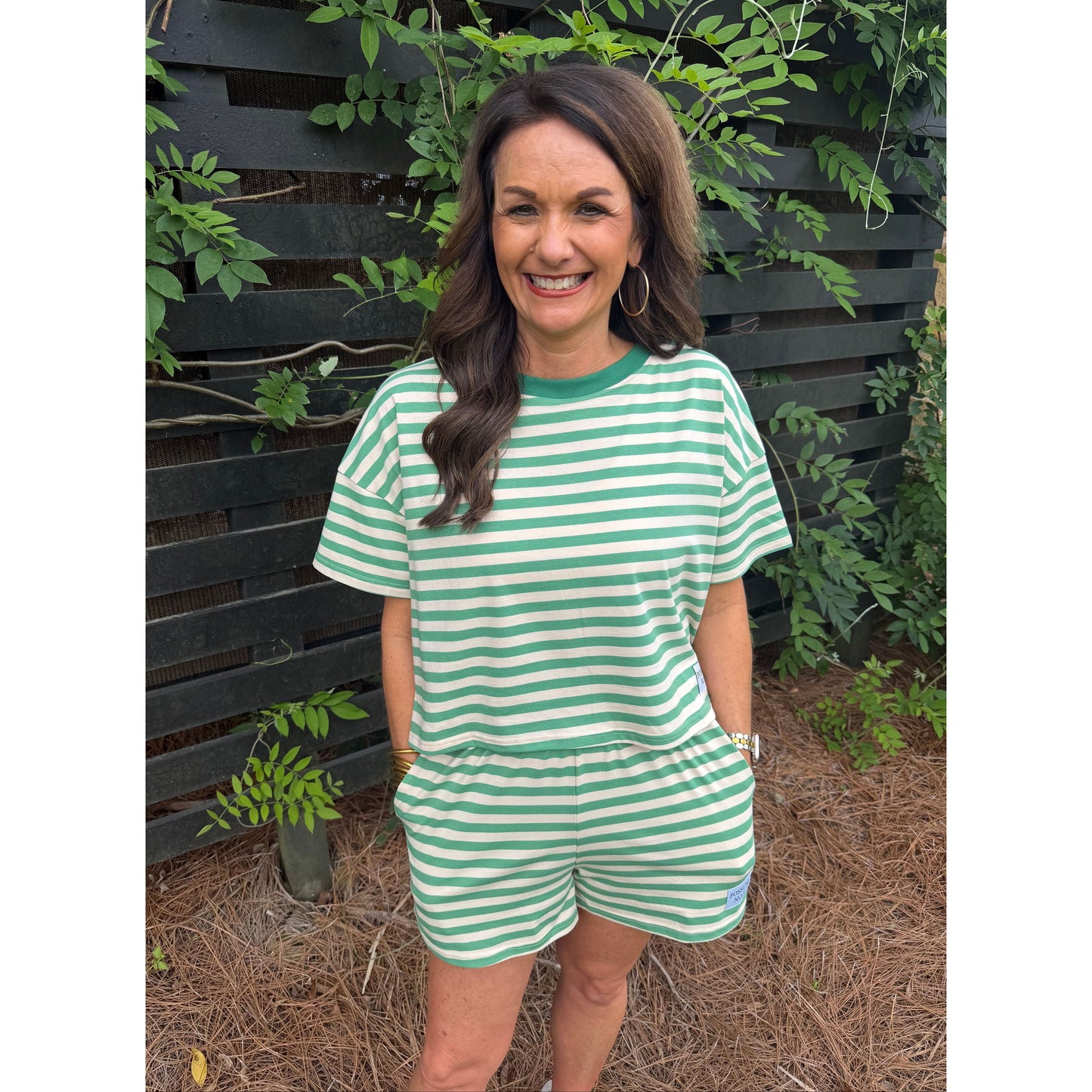 Woman wearing a green and white striped dress standing outdoors with plants around.