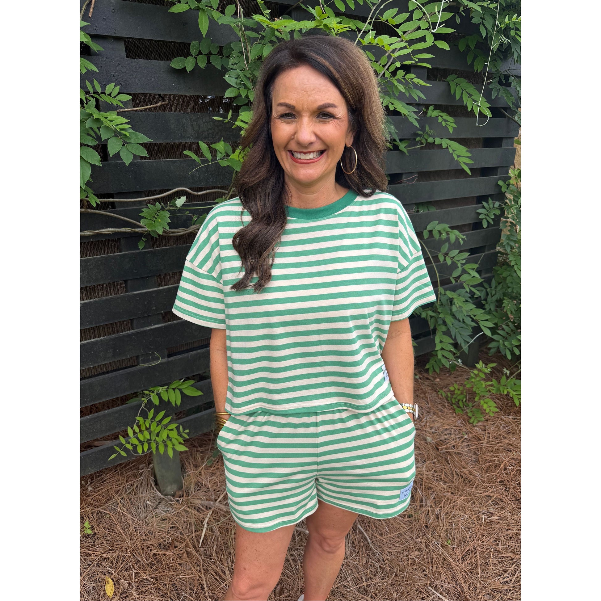 Woman wearing a green and white striped dress standing outdoors with plants around.