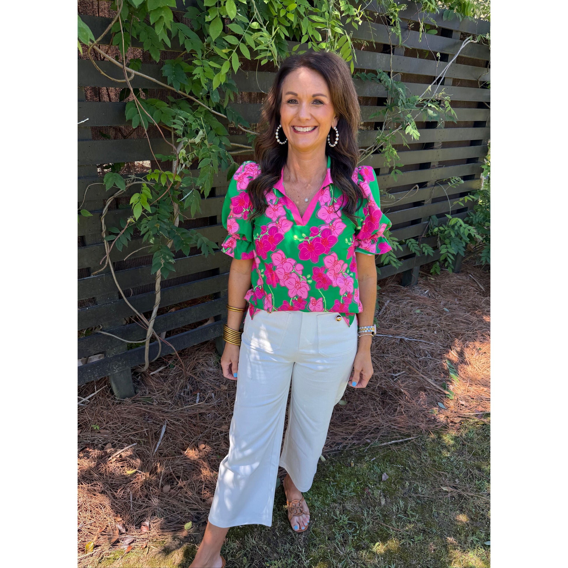 Woman wearing a colorful floral blouse and white pants standing outdoors.