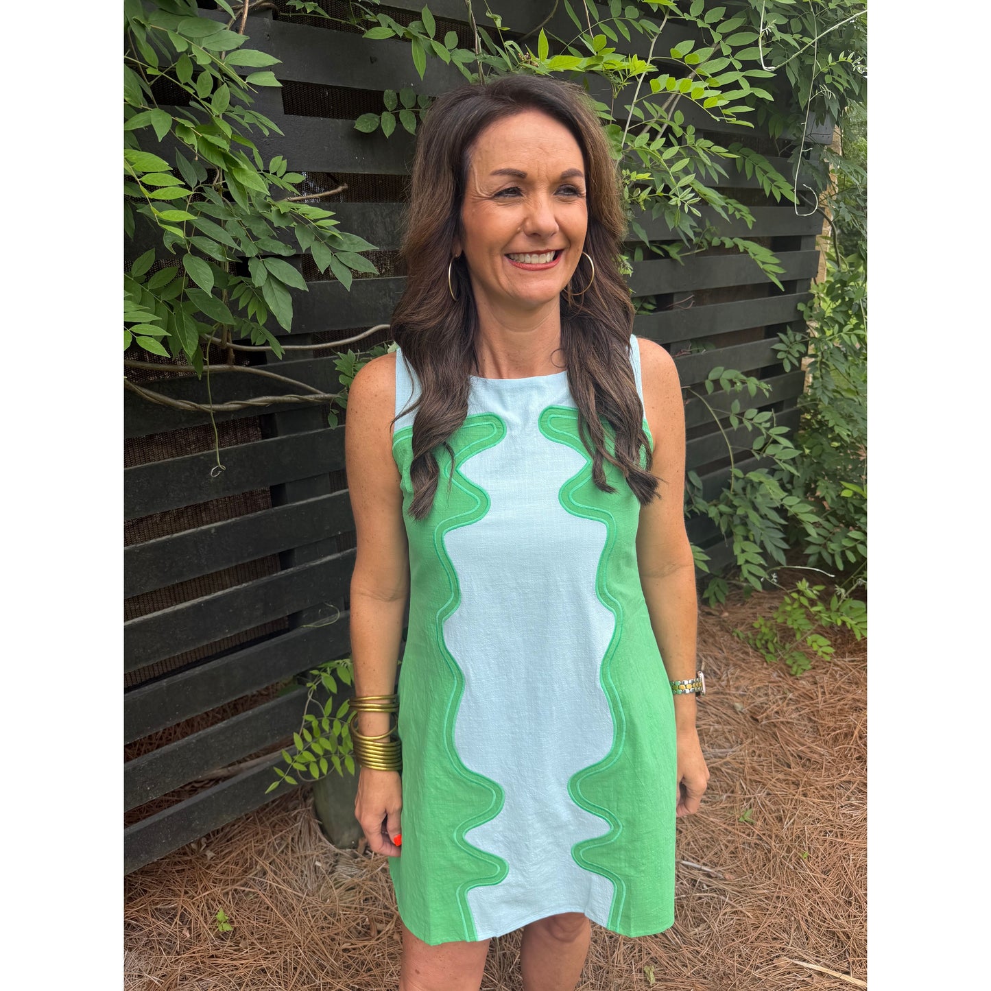 Woman wearing a green and white dress standing outdoors with greenery in the background