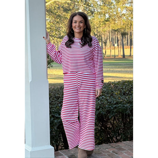 Woman wearing a red and white striped dress standing outdoors with trees and a brick wall in the background.