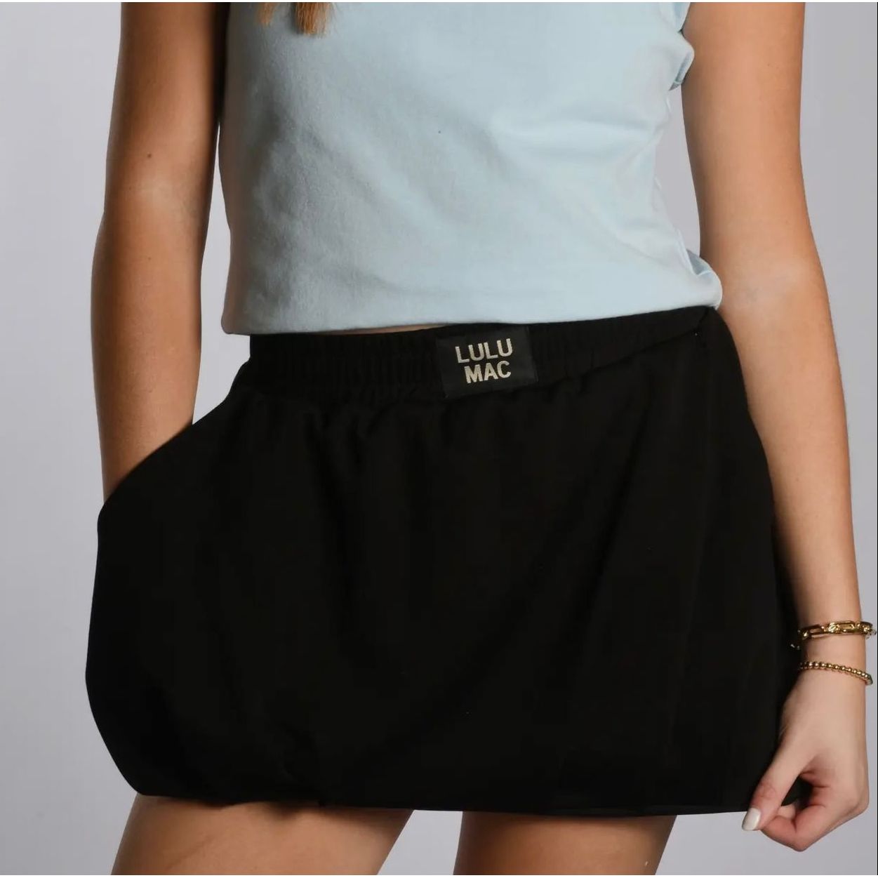 Person wearing a black Lulu Mac skirt with a light blue top on a plain background