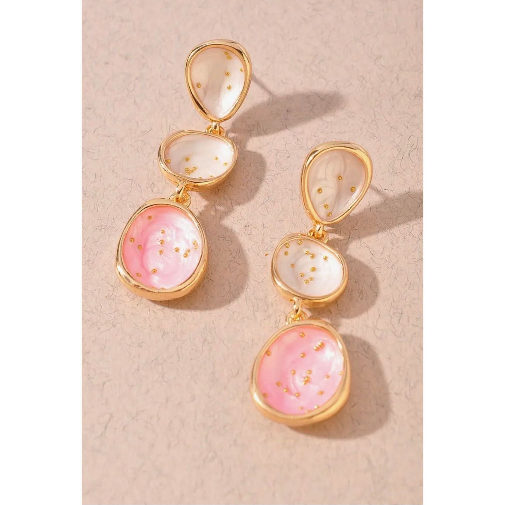 Gold earrings with pink and white stones on a beige background