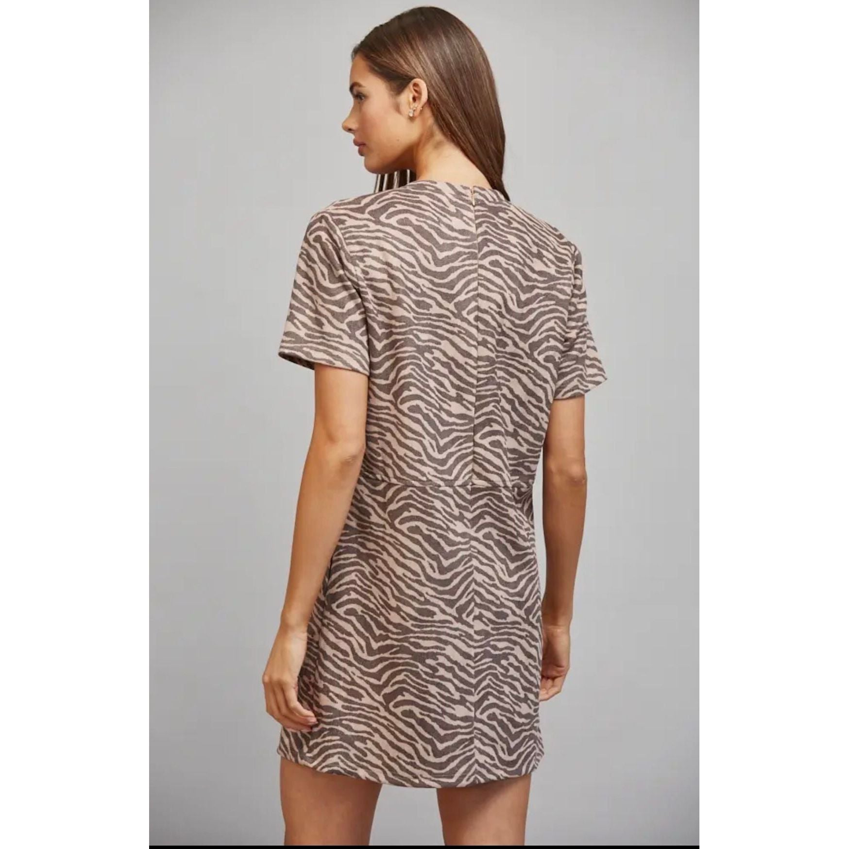 A woman shown from the back wearing a short-sleeve t-shirt dress with a brown and beige zebra print, set against a plain gray studio background.