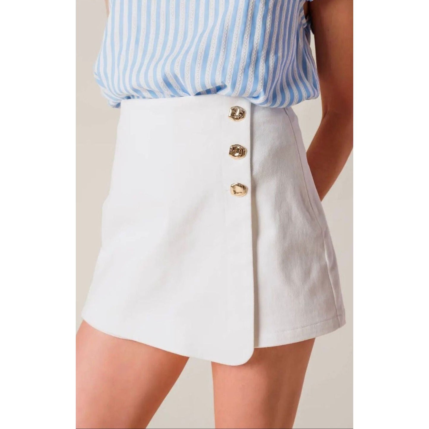 White skirt with gold buttons worn by a person against a neutral background