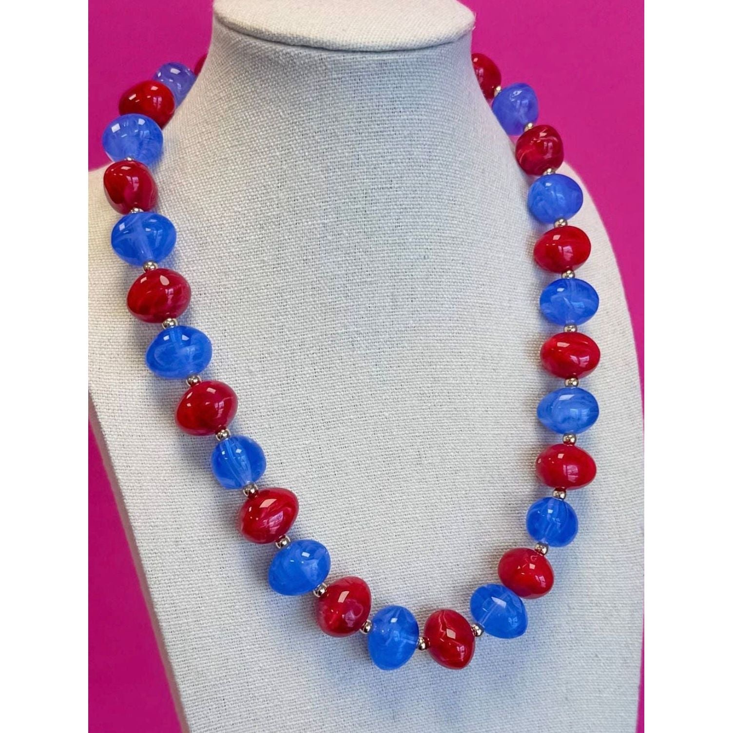 Necklace with red and blue beads on a mannequin against a pink background