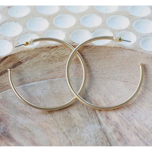 Gold hoop earrings on a wooden surface with a shell pattern in the background