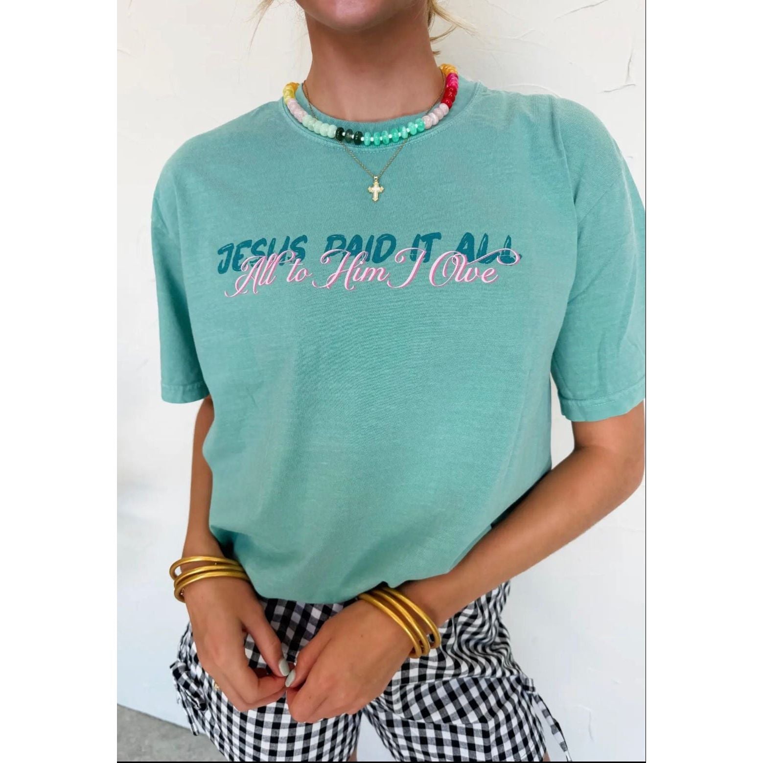 Person wearing a teal t-shirt with text, standing against a white background