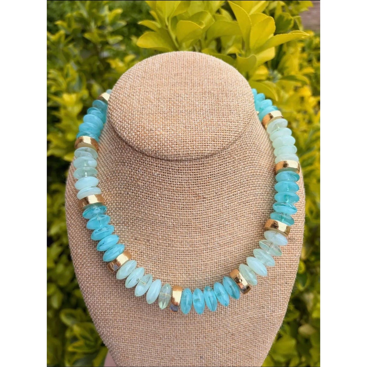 Necklace with blue beads on a beige bust against a green leafy background