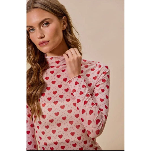 Woman wearing a pink sweater with red heart patterns against a beige background
