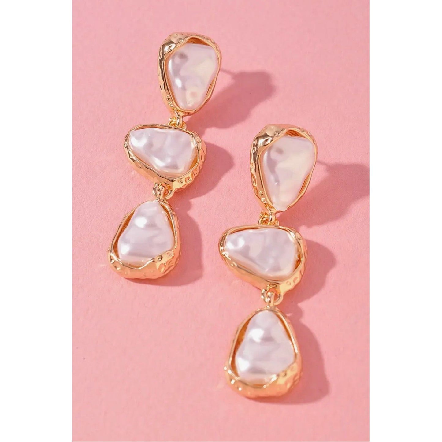 Gold and pearl drop earrings on a pink background