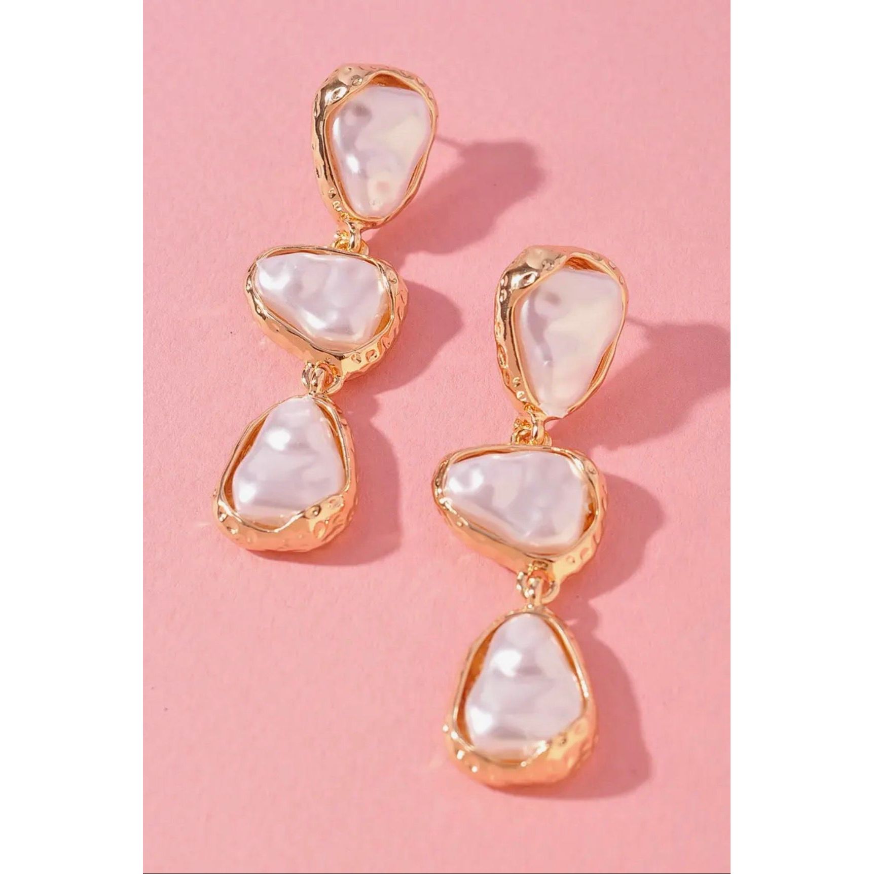 Gold and pearl drop earrings on a pink background