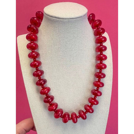 Red beaded necklace on a mannequin bust against a pink background