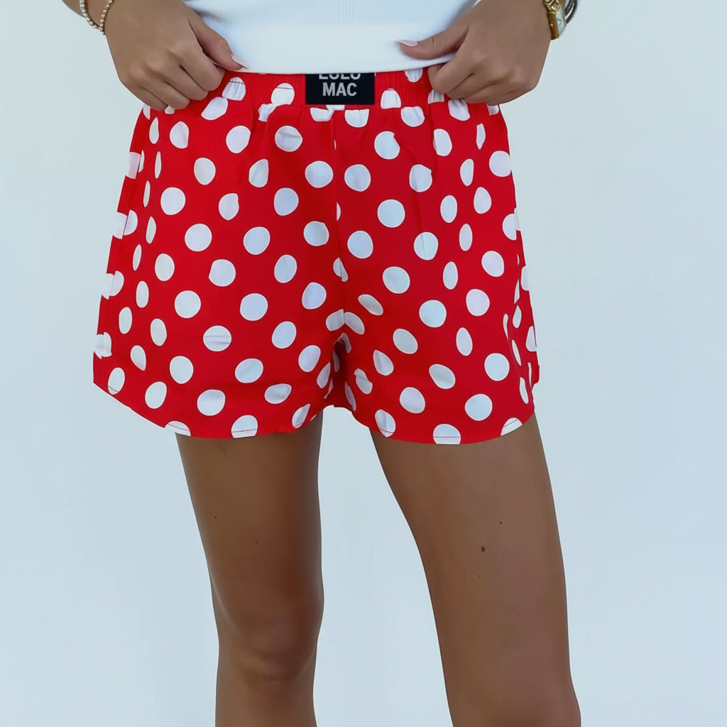 Red polka dot shorts worn by a person against a white brick wall.