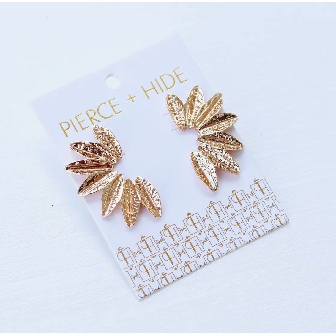 Gold leaf-shaped earrings on a Pierce + Hide card against a light gray background