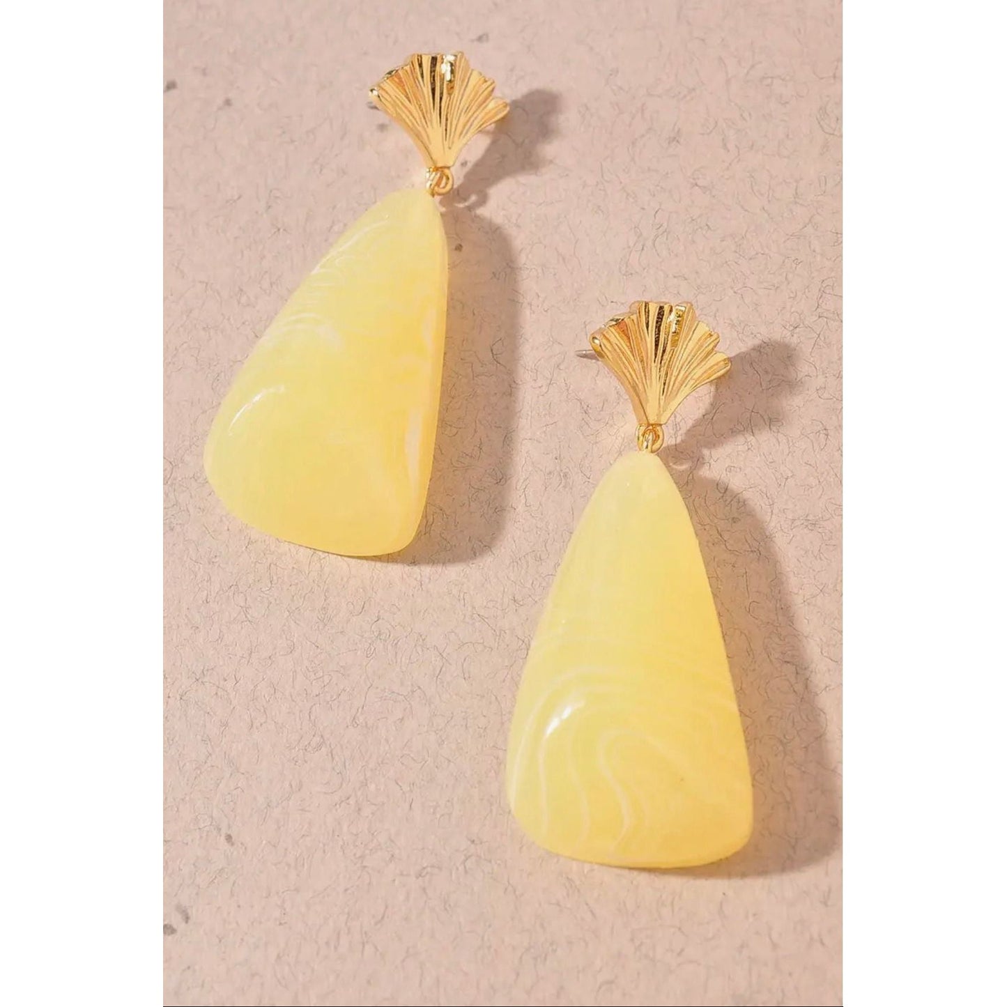 Pair of yellow teardrop earrings with gold tops on a beige background