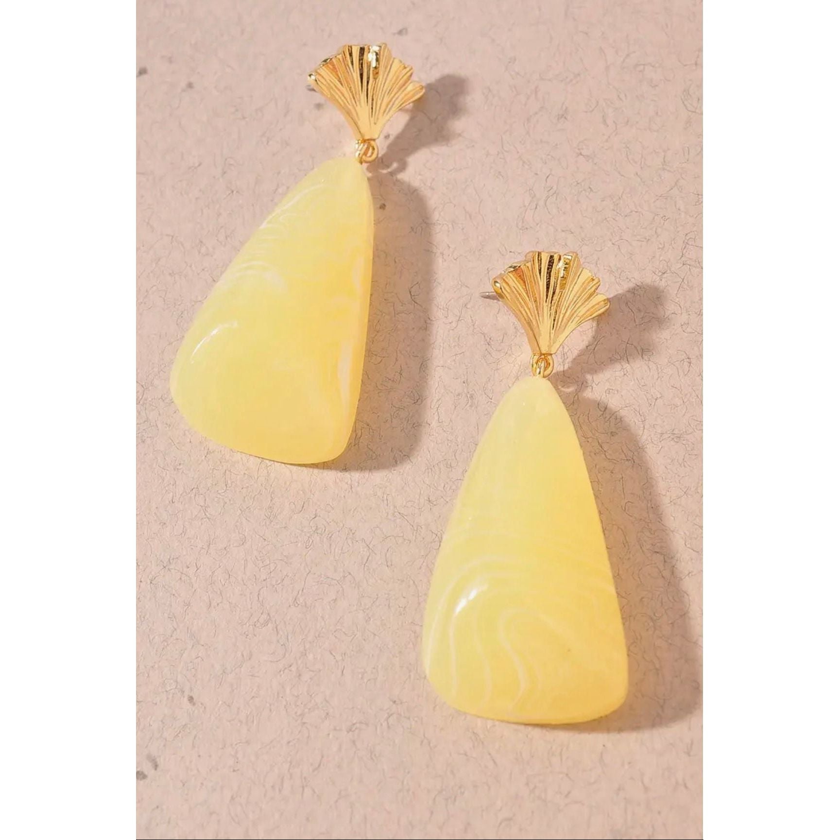 Pair of yellow teardrop earrings with gold tops on a beige background