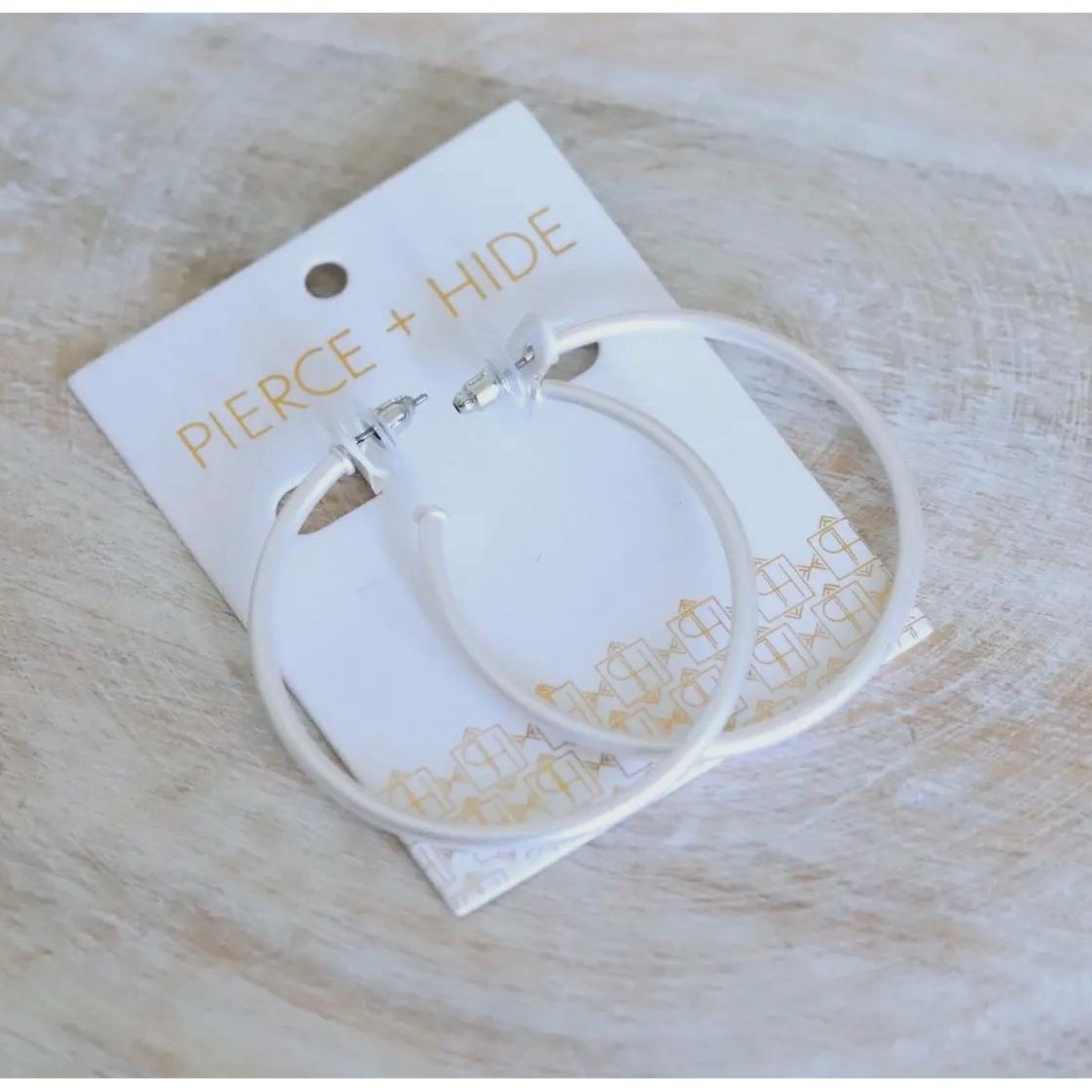 Silver hoop earrings on a Pierce + Hide branded card with a light wooden background