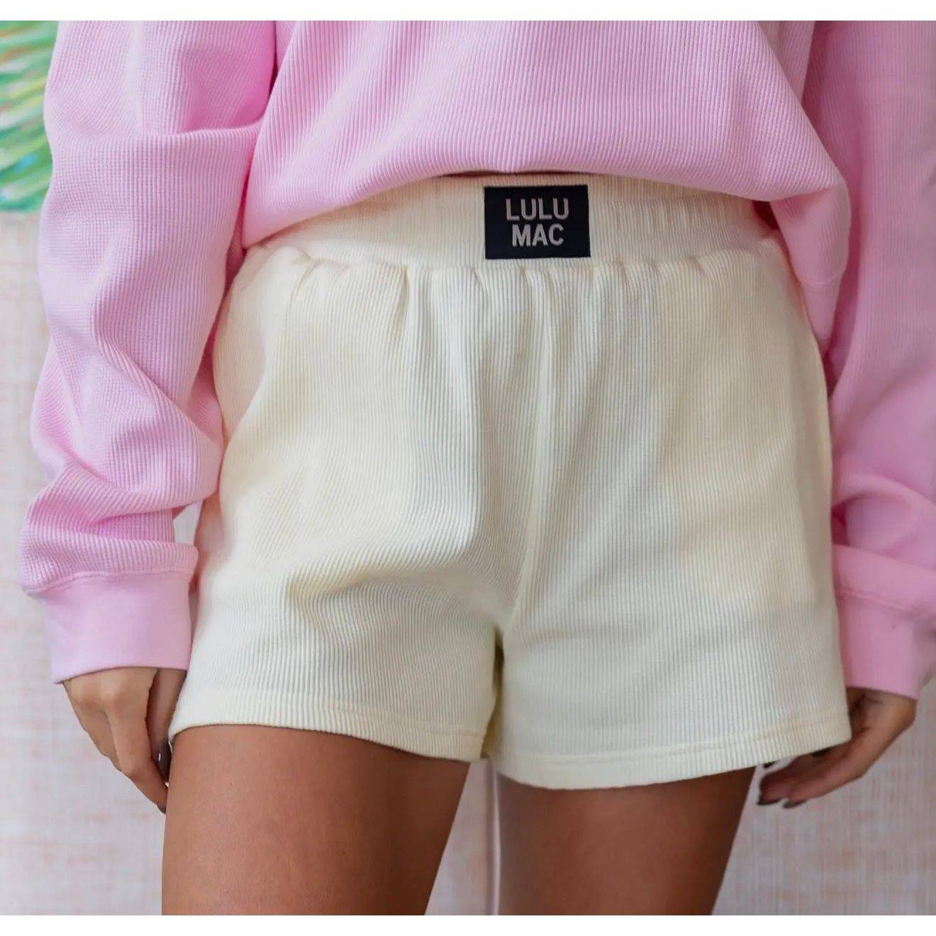 Person wearing a pink sweatshirt and cream shorts with 'LULU MAC' branding.
