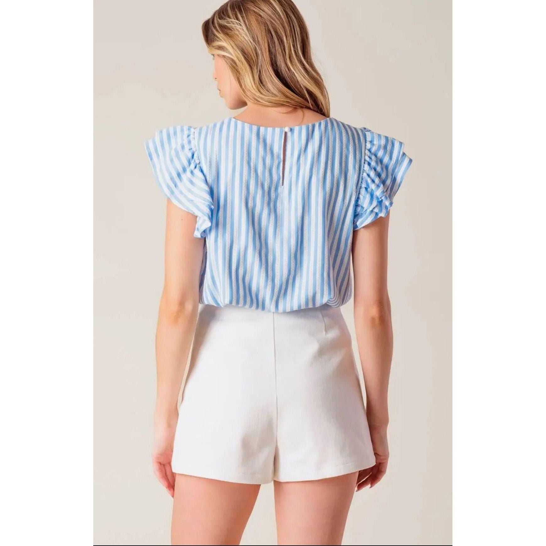 Woman wearing a blue and white striped top and white shorts on a plain background