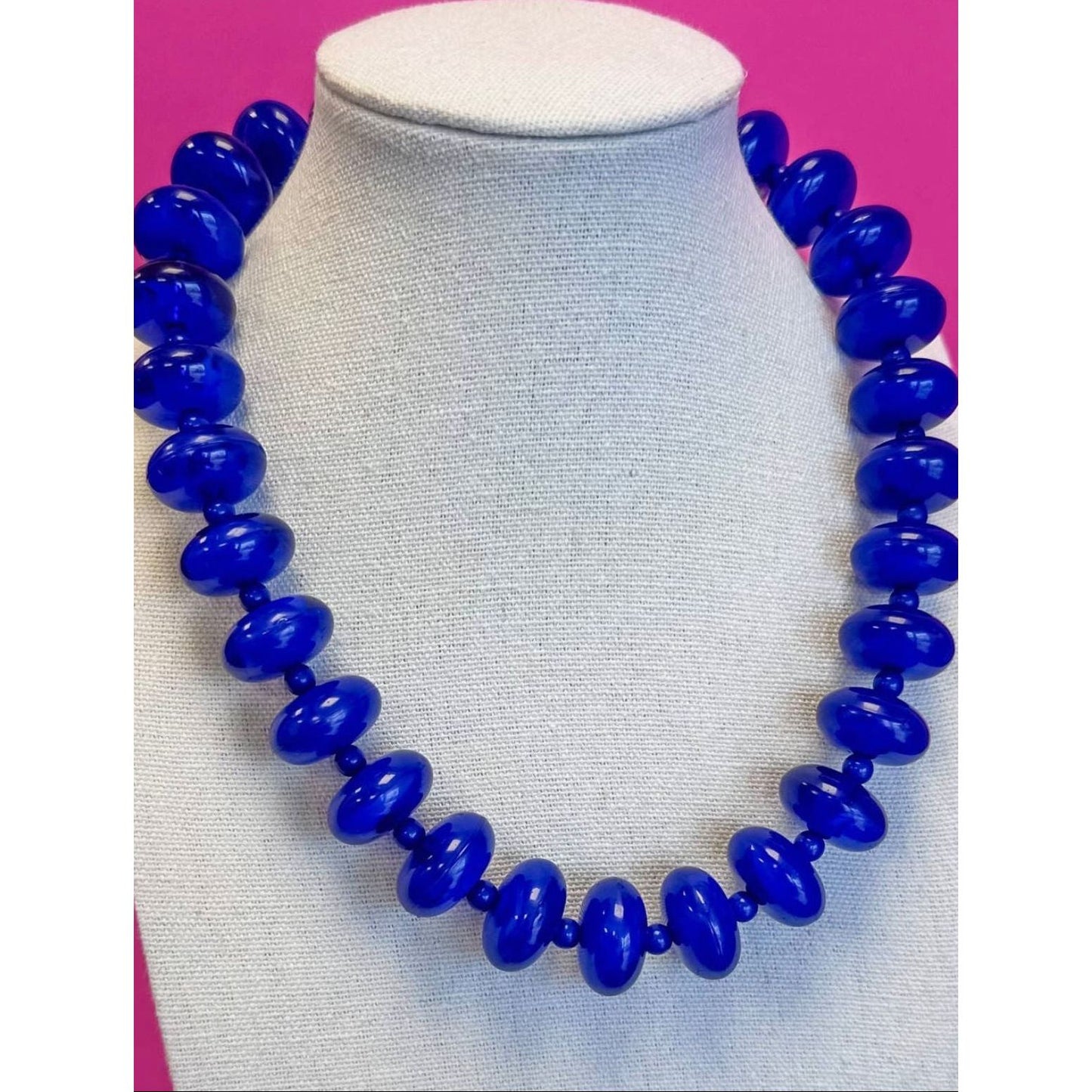 Blue beaded necklace on a mannequin against a pink background