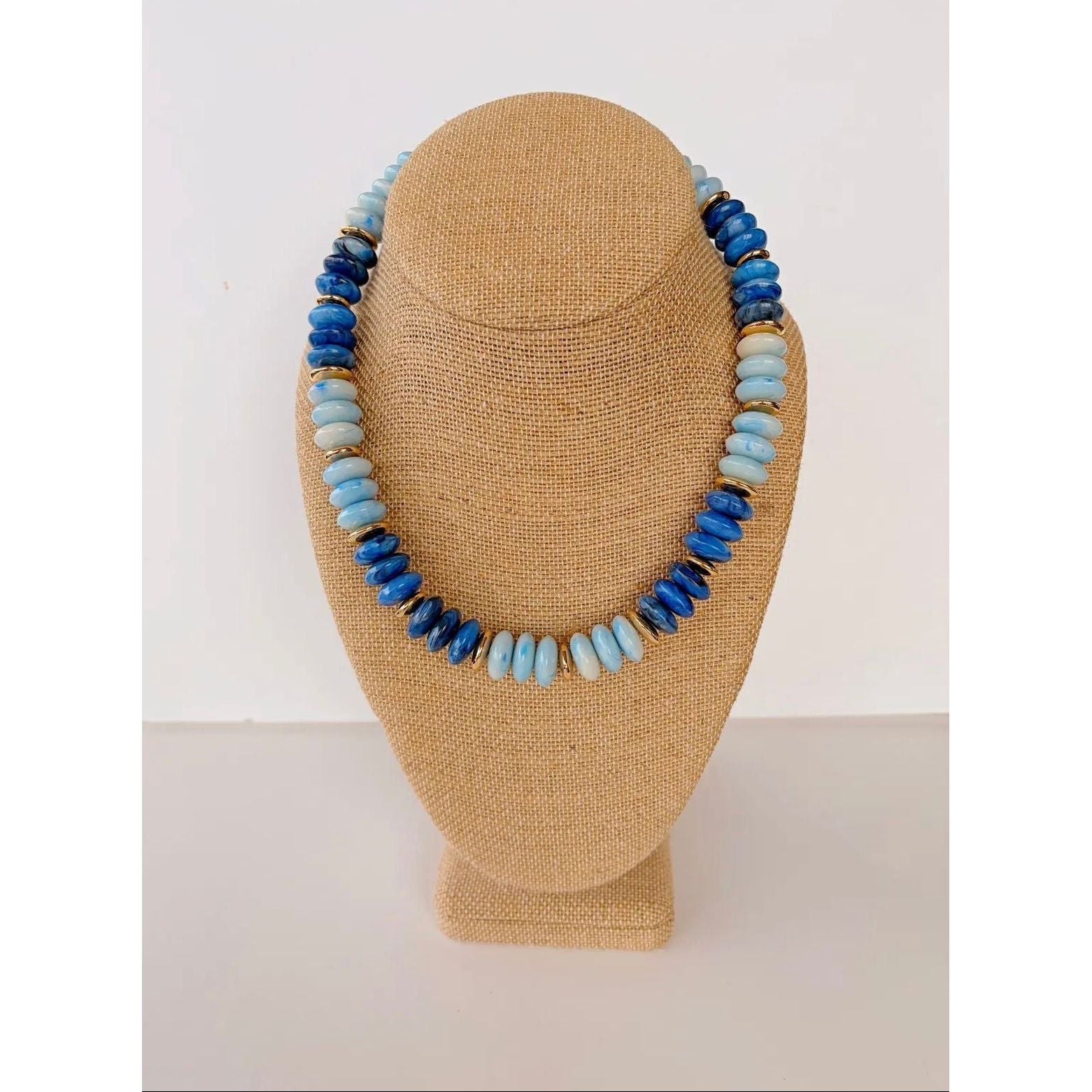 Necklace with blue and light blue beads on a tan mannequin bust against a white background
