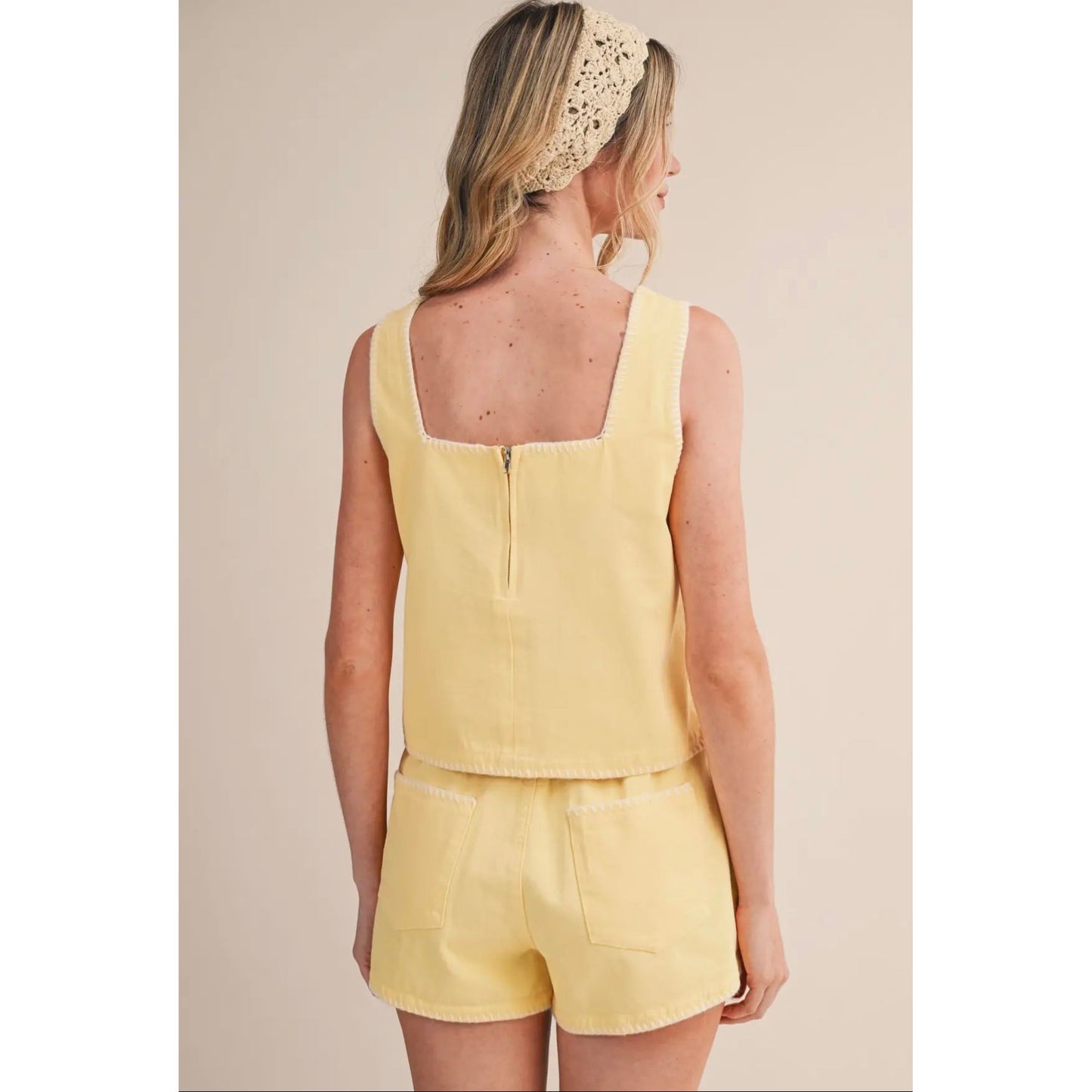 Woman wearing a yellow sleeveless top and shorts set on a beige background
