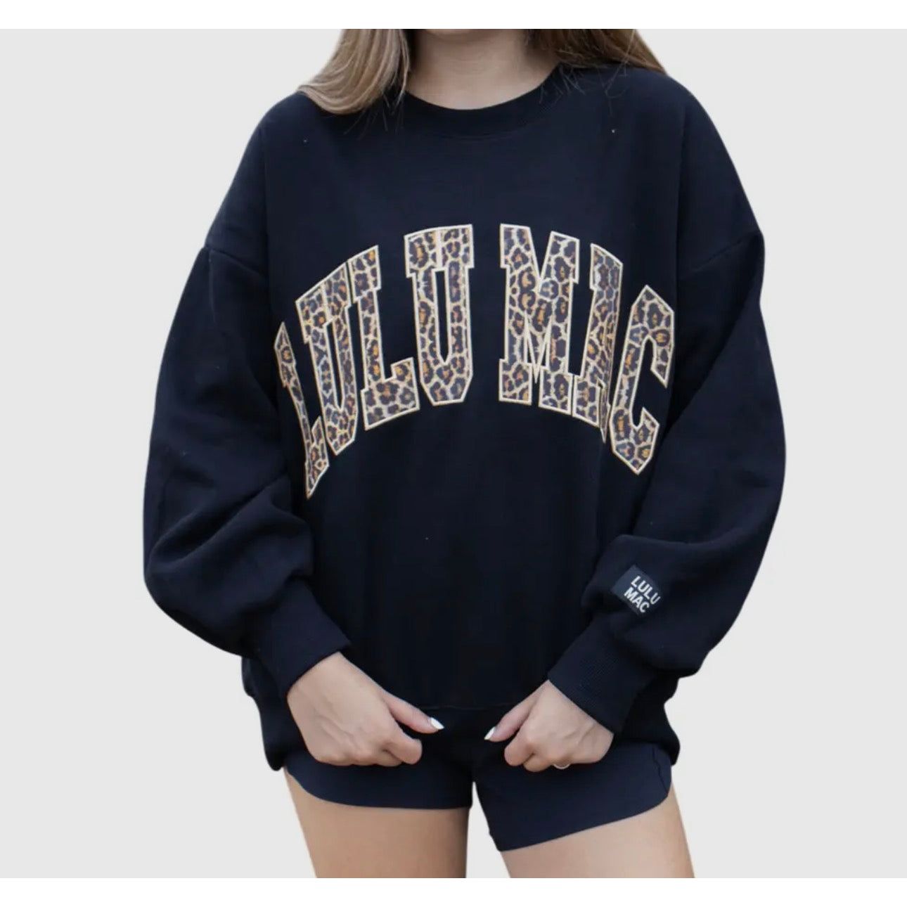 Person wearing a navy blue sweatshirt with 'LULUMAC printed in leopard print on a plain background