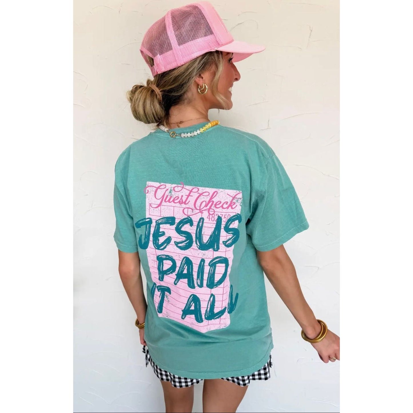 Person wearing a teal t-shirt with a graphic design and a pink cap against a white background
