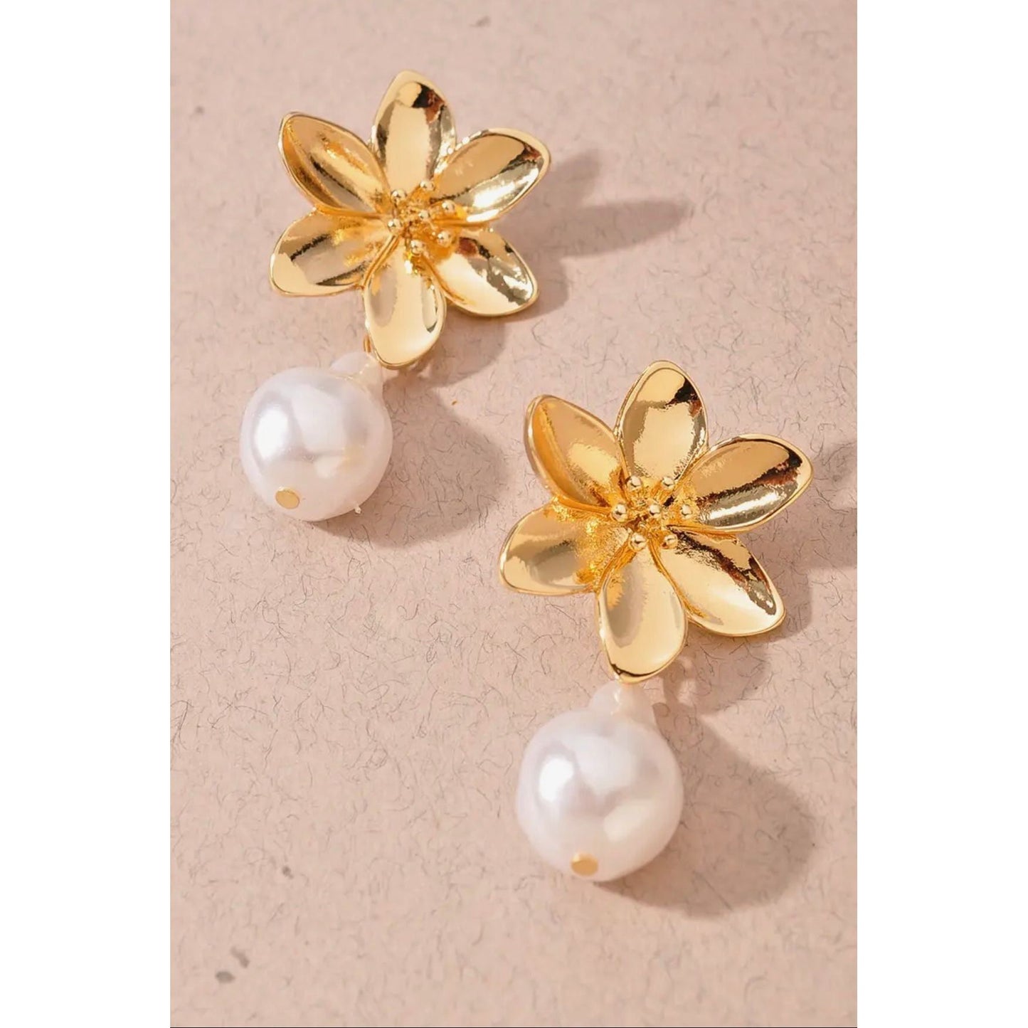 Gold flower-shaped earrings with pearl drops on a beige background